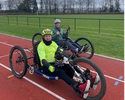 Two people riding hand cycles on a running track