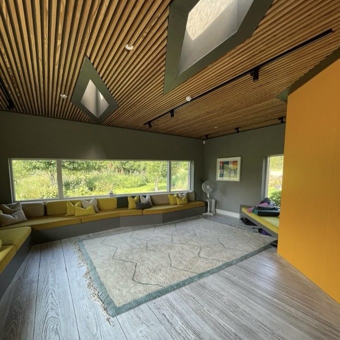 A bright, open room at Maggie's Centre Forth Valley with a rug, window seating and skylights in a timber ceiling.