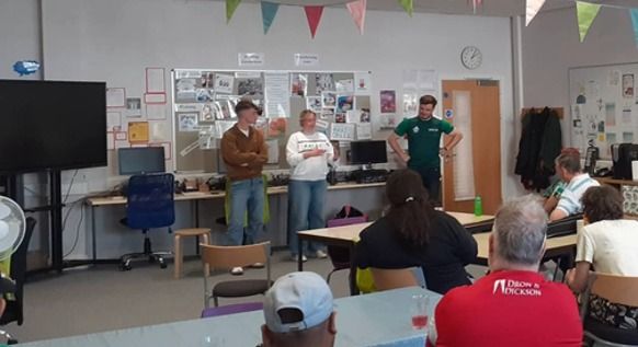 A student presenting to a seated group in a community room.